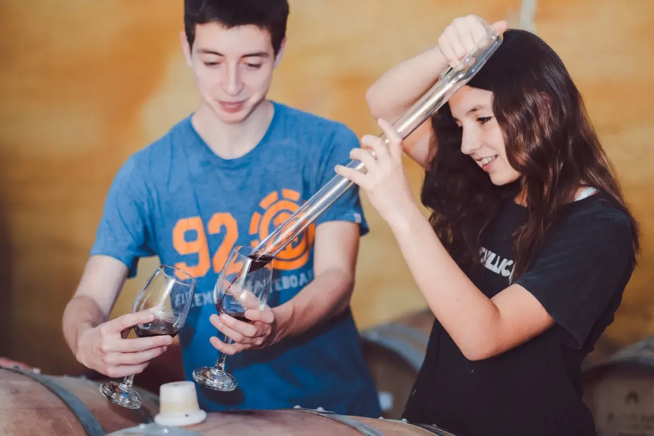 Two young people drawing wine from a barrel with a pipette during a cellar tasting